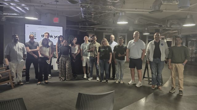 A diverse group of meetup attendees standing together facing the camera in front of a thank-you slide on a large screen.